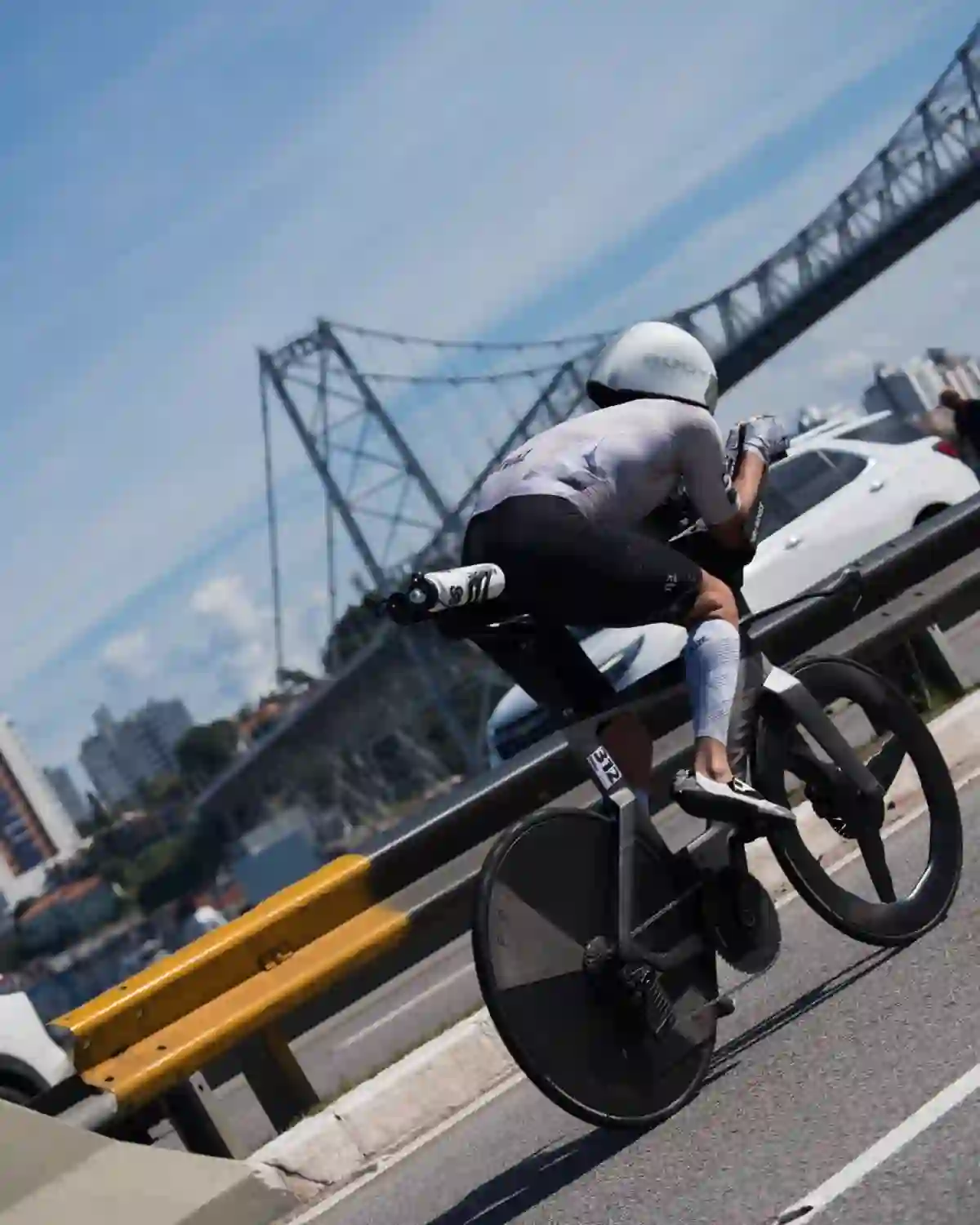 Atleta em posição aero na bike de prova, com a ponte Hercílio Luz ao fundo, em Florianópolis