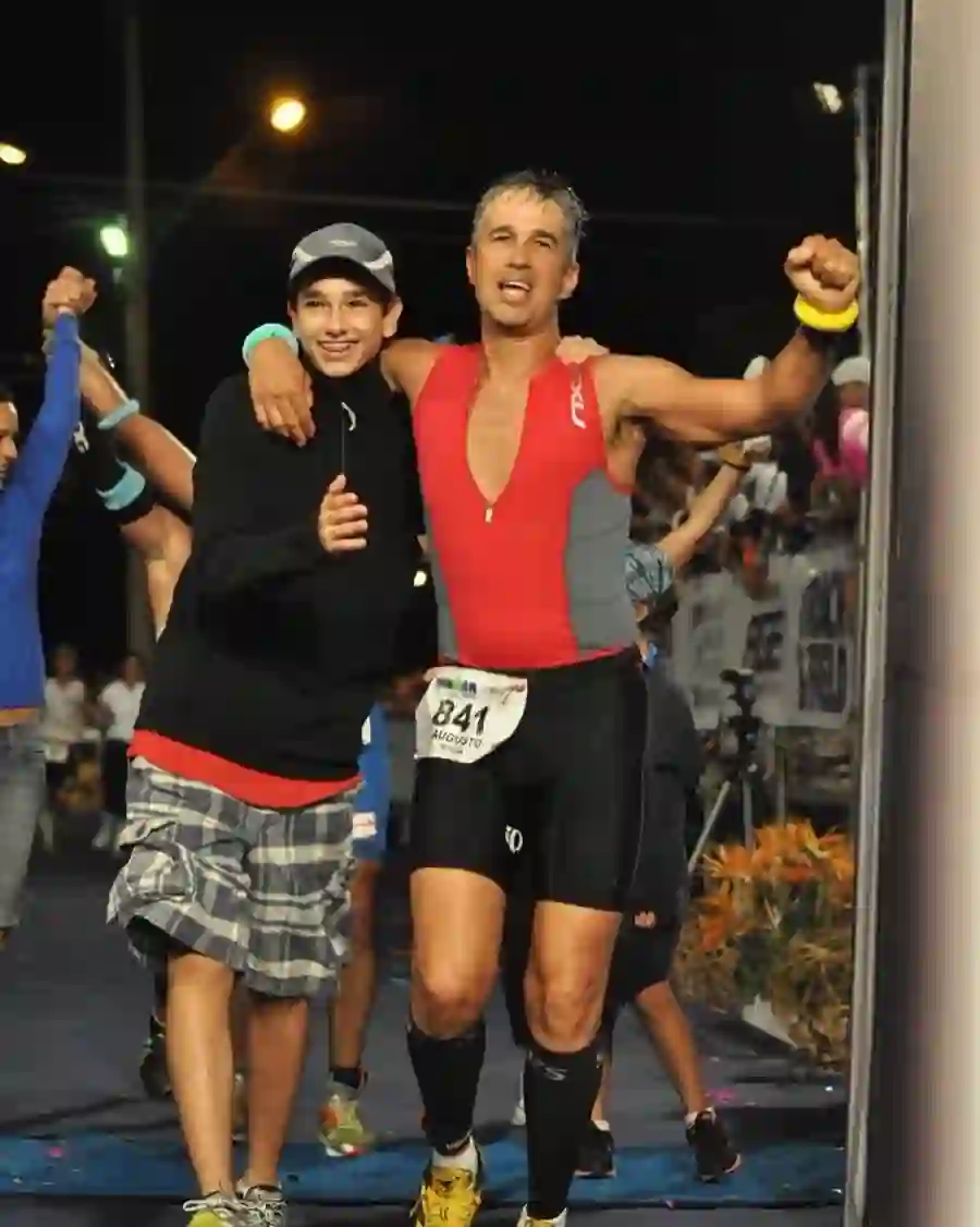 Gui Vaz ainda adolescente, ao lado do pai, na chegada de uma prova de Ironman à noite